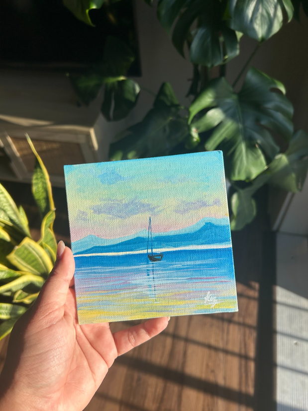 Anchored in Stillness — a mini painting of a sailboat on calm blue water, held in hand