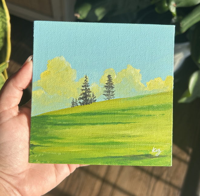 Sunlit Hills — a green hillside with pines under a bright blue sky, hand-painted on a small square canvas panel, held in hand